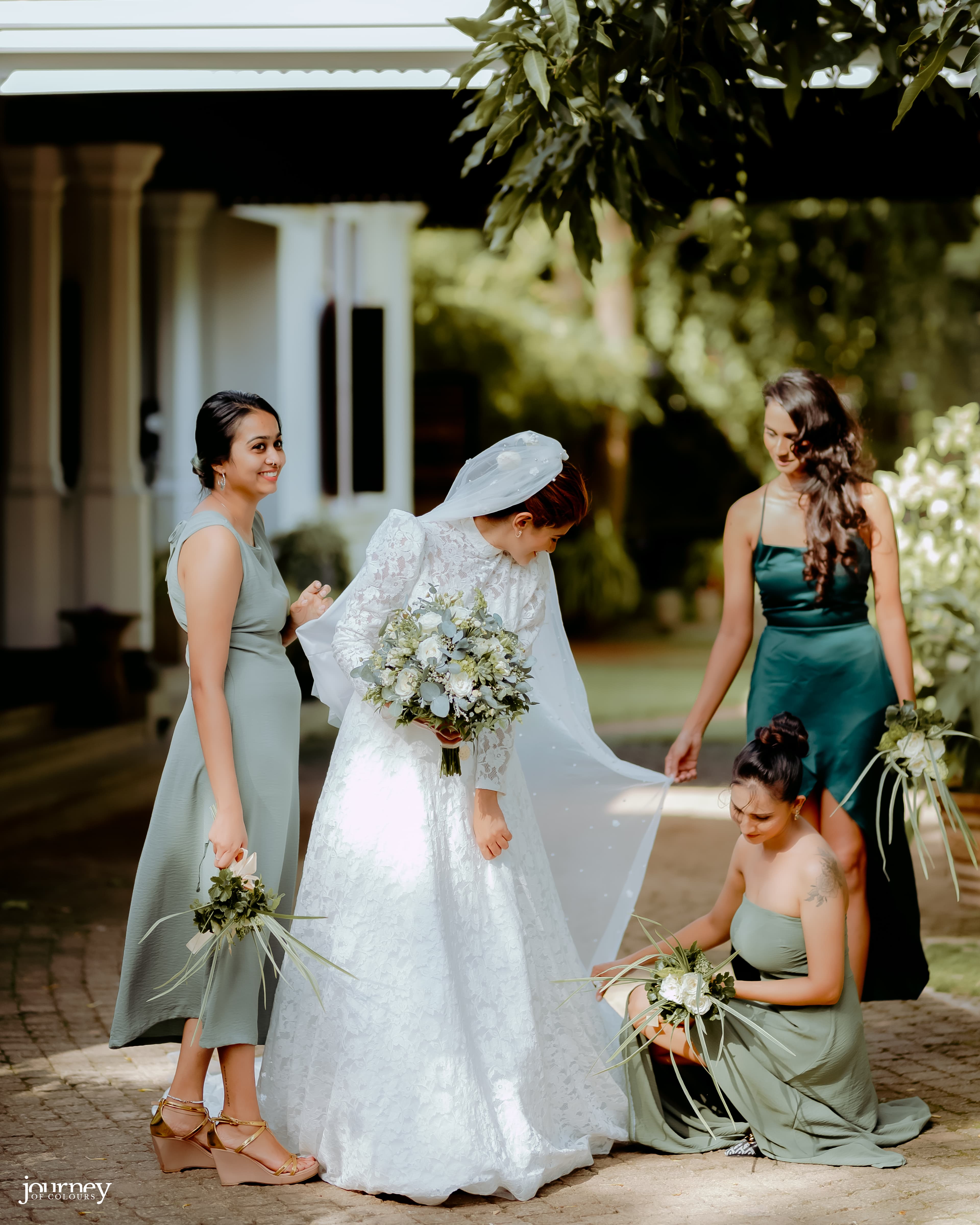 Bride looking down as her bridesmaids make final adjustments to her gown